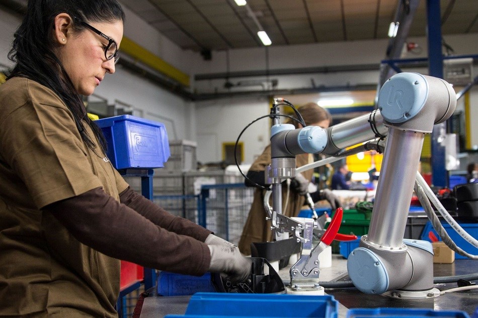 Eine Frau und ein kollaborierender Roboterarm arbeiten Seite an Seite.