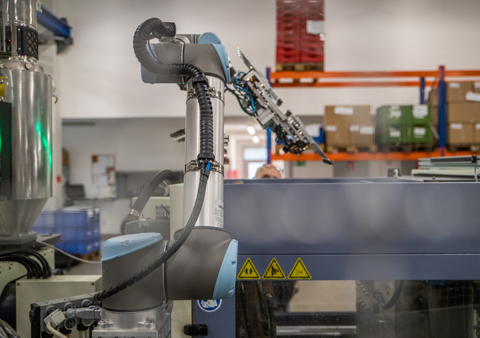 Ein kollaborierender Roboterarm arbeitet zwischen einer Pressmaschine und einem Förderband, um die Maschine zu beladen.