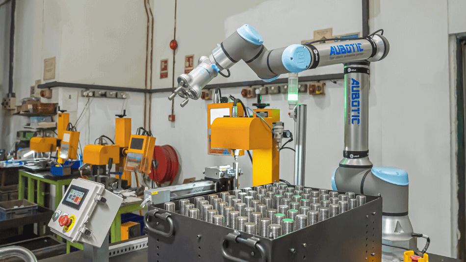 Ein Roboterarm mit elektrischem Greifer steht neben einem Tray mit Metallteilen.