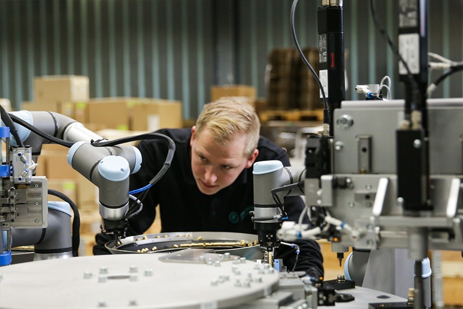 Ein junger Mann betrachtet konzentriert einen kollaborierenden Roboterarm, der an einer Maschine arbeitet.