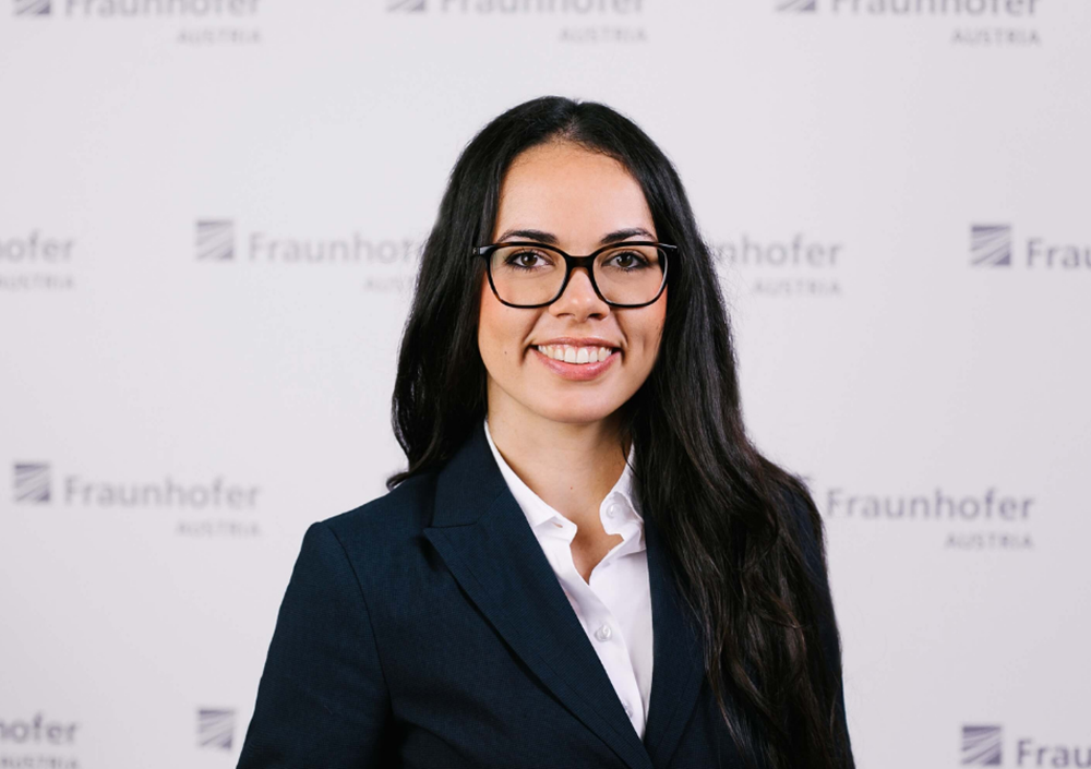 Das Bild zeigt Titanilla Komenda vom Fraunhofer Institut. Die dunkelhaarige junge Frau trägt eine Brille und lächelt in die Kamera.