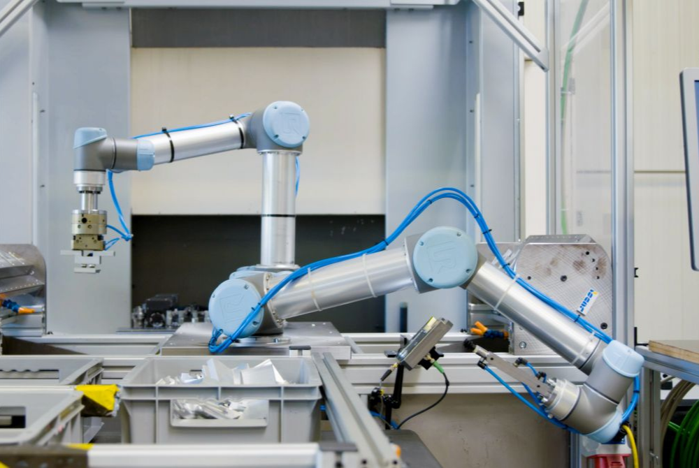 Zwei kollaborierende Roboterarme von Universal Robots bestücken eine CNC-Fräse mit Metallteilen zur Verarbeitung.