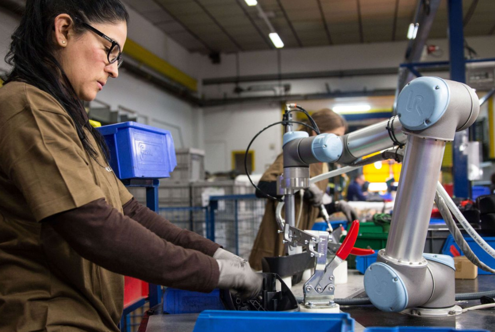 Eine Frau und ein kollaborierender Roboterarm arbeiten Seite an Seite.