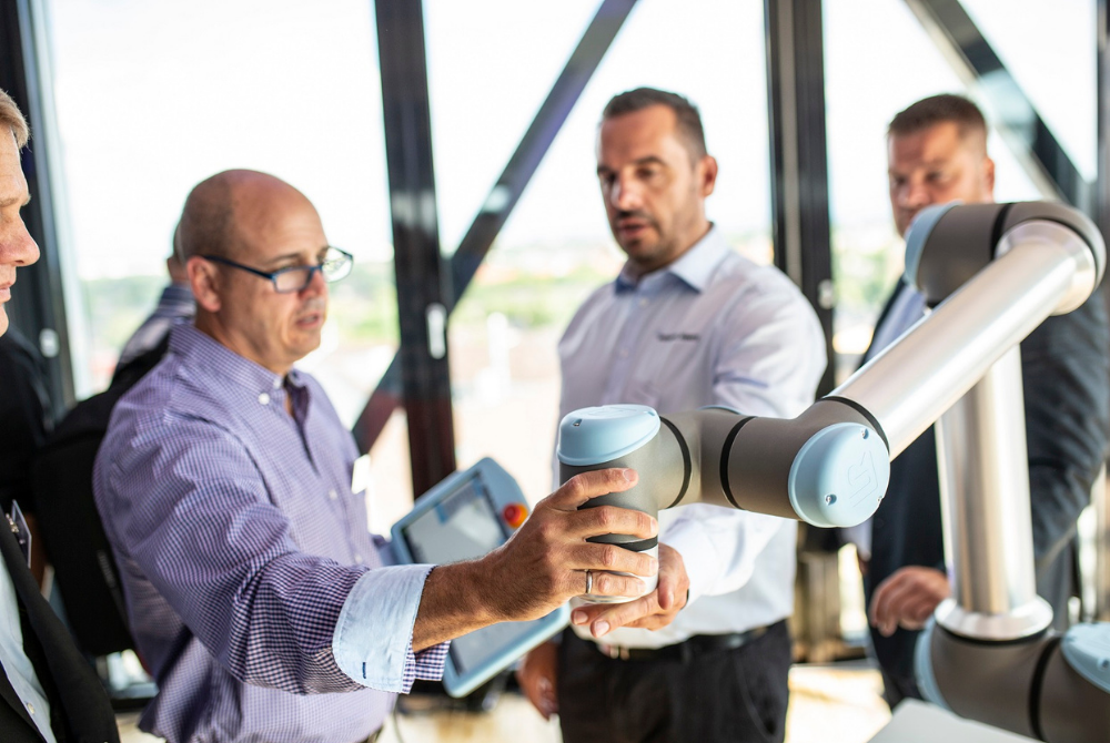 Zwei Männer halten den Toolflansch eines Cobots in der Hand. Einer von ihnen hält das Bedienpanel. Der andere erklärt ihm etwas.