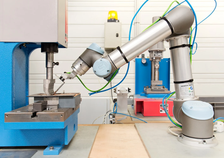 Ein kollaborierender Roboterarm bestückt eine Falzmaschine mit einem Metallteil.