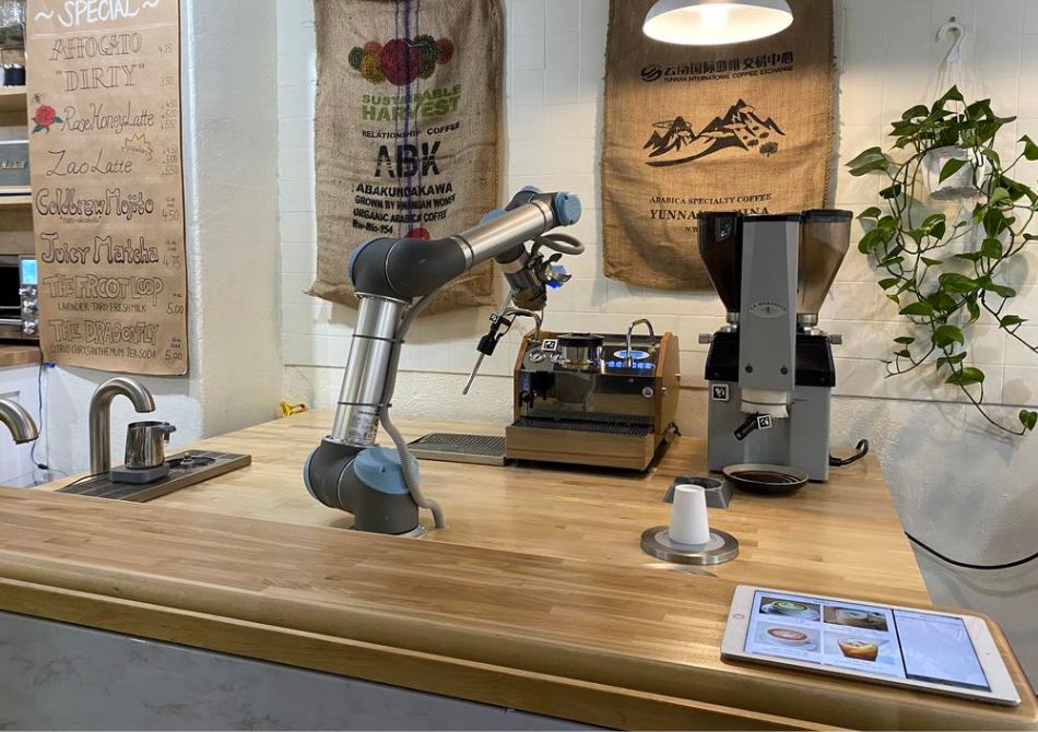 Ein kollaborierender Roboterarm bedient eine Espressomaschine und eine Kaffeemühle an einem Holztresen.