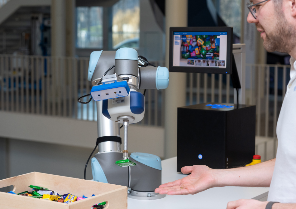 Ein Mann streckt seine Hand nach einem kollaborierenden Roboterarm aus, der eine Schokoladentafel mit einem Vakuumgreifer hält.