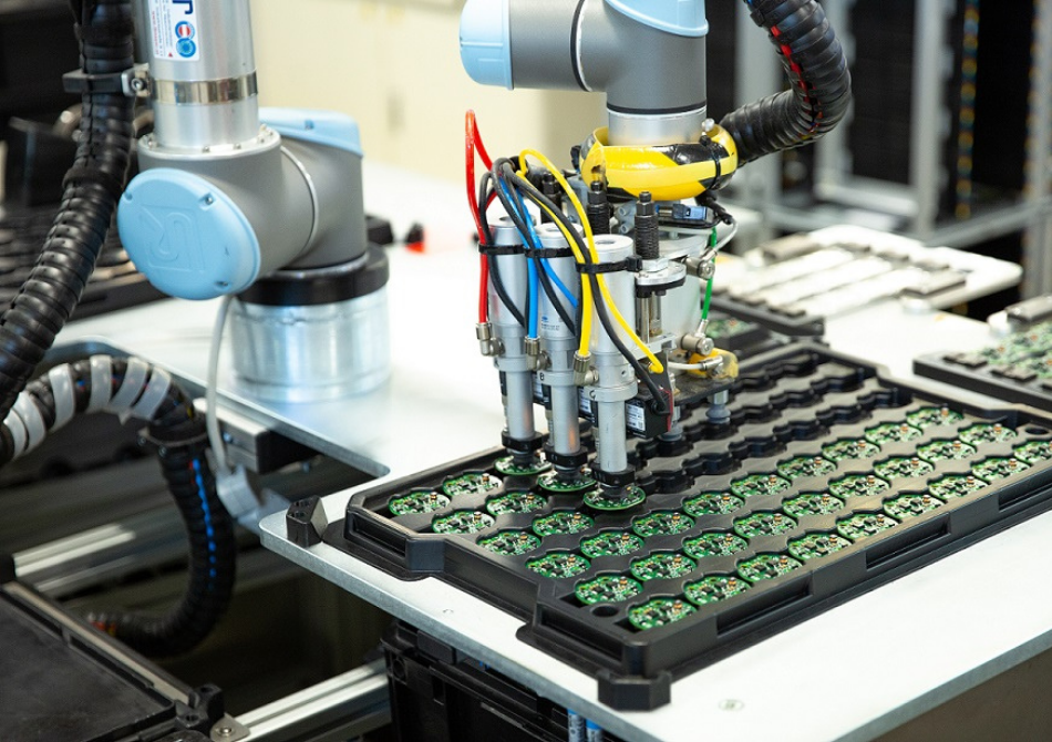 Ein Cobot greift mit einem Sauggreifer drei Leiterplatten gleichzeitig und platziert sie in einem Tray.