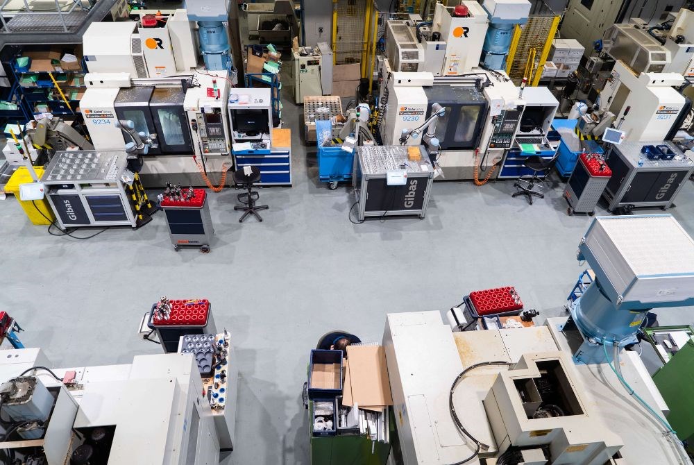 Das Bild zeigt eine Werkshalle mit zahlreichen CNC Fräsen, die aufgereiht an einem Gang stehen. An einige Maschinen stehen kollaborierende Roboterarme.
