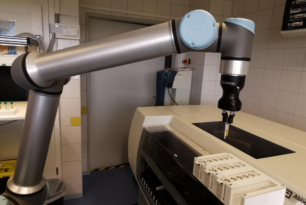 Ein kollaborierender Roboterarm steht in einem Labor und nimmt eine Blutprobe aus einem Register auf.