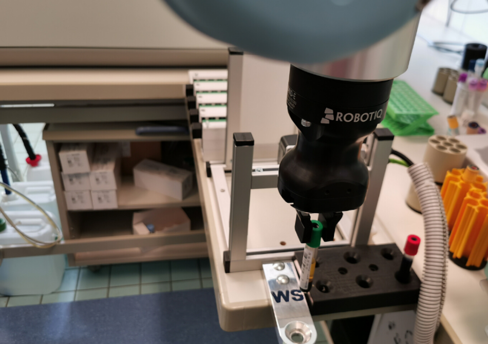 Ein Backengreifer von Robotiq angebracht an einem Cobot hält eine Blutprobe in einem Labor.