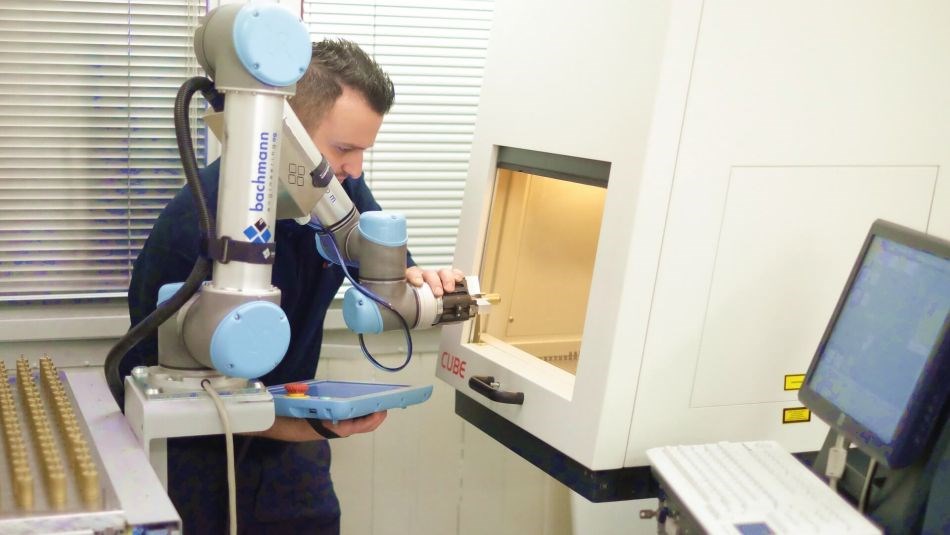 Ein Mann führt einen kollaborierenden Roboterarm in eine Werkzeugmaschine.