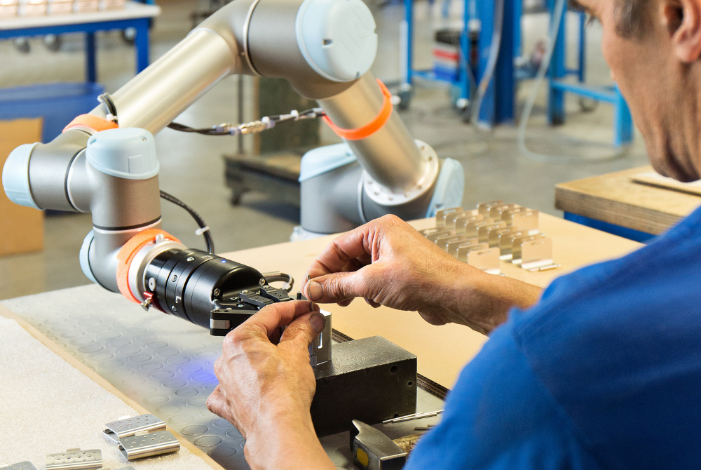 Ein Mann arbeitet gemeinsam mit einem kollaborierenden Roboterarm an einem Werkstück.