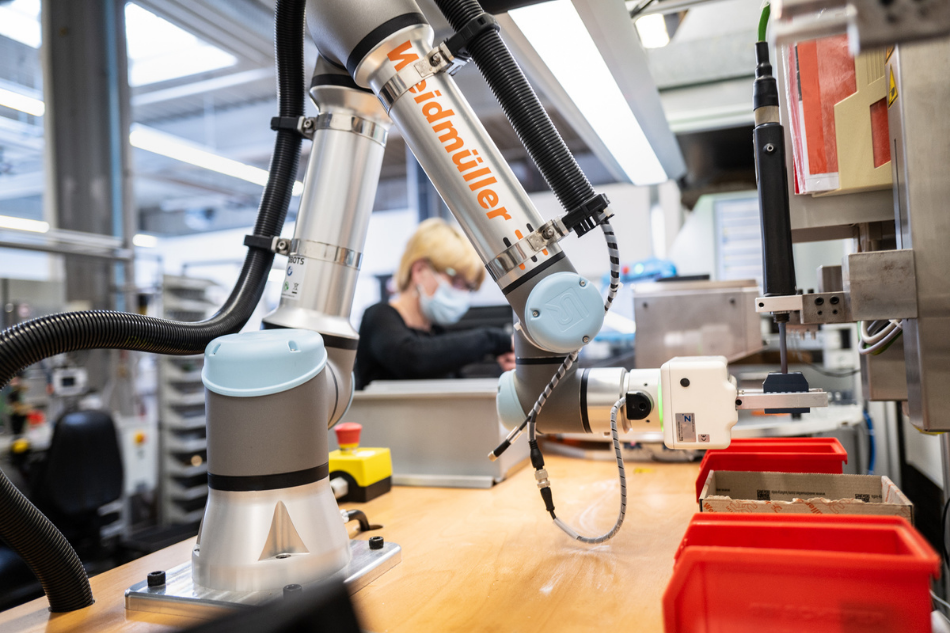 Der kollaborierende Roboter hilft dem Menschen an einem hybriden Arbeitsplatz in der Elektronikfertigung bei der Montage von Werkstücken und entlastet die Mitarbeitenden so von monotonen und kraftintensiven Aufgaben.