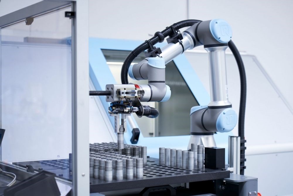Ein kollaborierender Roboterarm nimmt Werkstücke auf und positioniert sie präzis in einem Tray vor einer CNC Fräsmaschine.