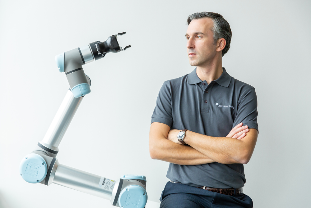 Der General Manager Western Europe Andrea Alboni lehnt neben einem Cobot und schaut in dessen Richtung.