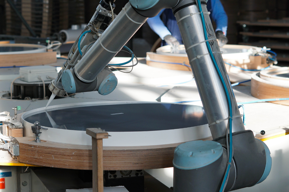 Ein kollaborierender Roboter (sog. Cobot) von Universal Robots trägt mit einer Klebepistole Klebstoff auf den Spiegelrahmen auf