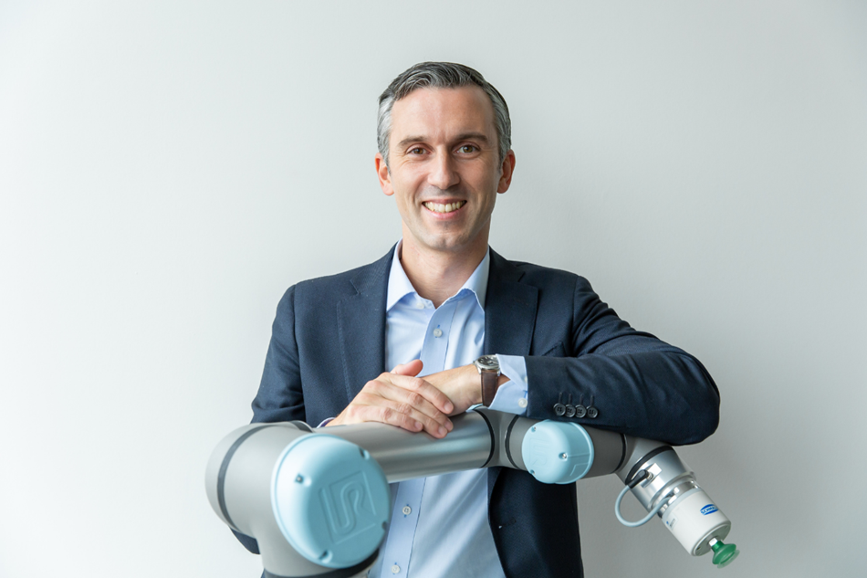 Andrea Alboni lächelt in die Kamera und legt seine Arme auf einen Cobot von Universal Robots.