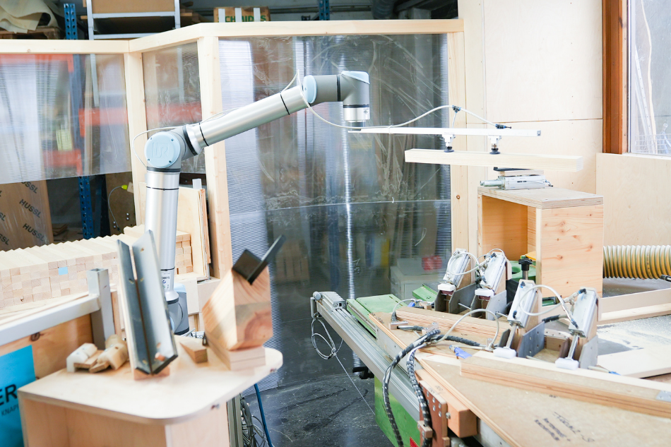 Ein mit einem Kraftsensor ausgestatteter Cobot greift empfindliche Holzteile für die weitere Bearbeitung in einer Tiroler Schreinerwerkstatt.