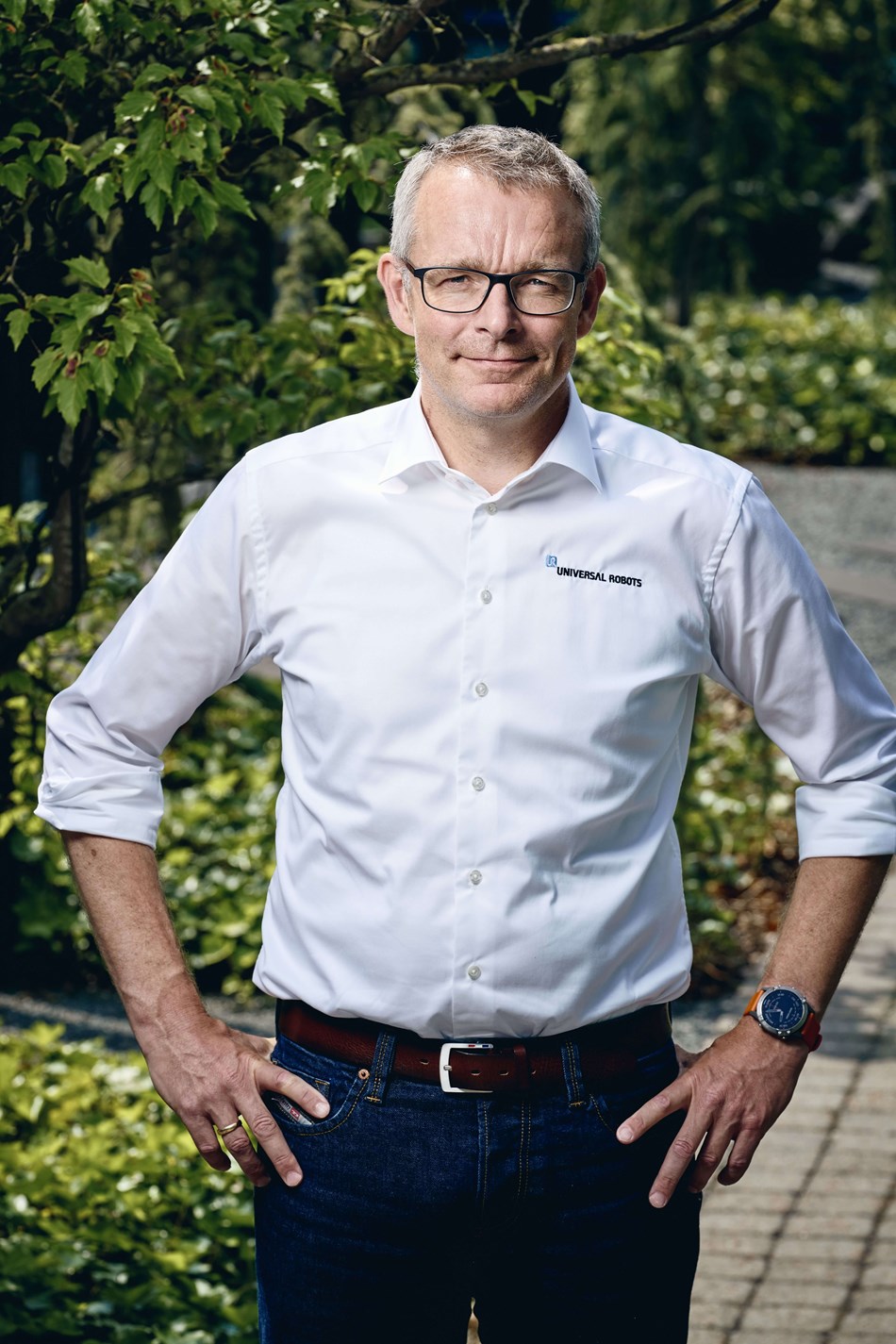 Man sieht hier Kim Nørgaard Andreasen, CFO bei Universal Robots. Er hat eine Brille an und posiert zu Kamera mit seinen Händen an seinen Hüften.