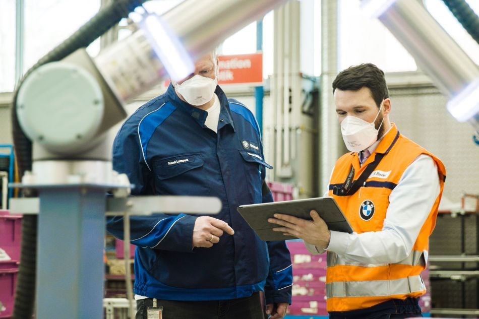 Zwei Männer mit Tablet stehen vor einem kollaborierender Roboter, um diesen zu programmieren.