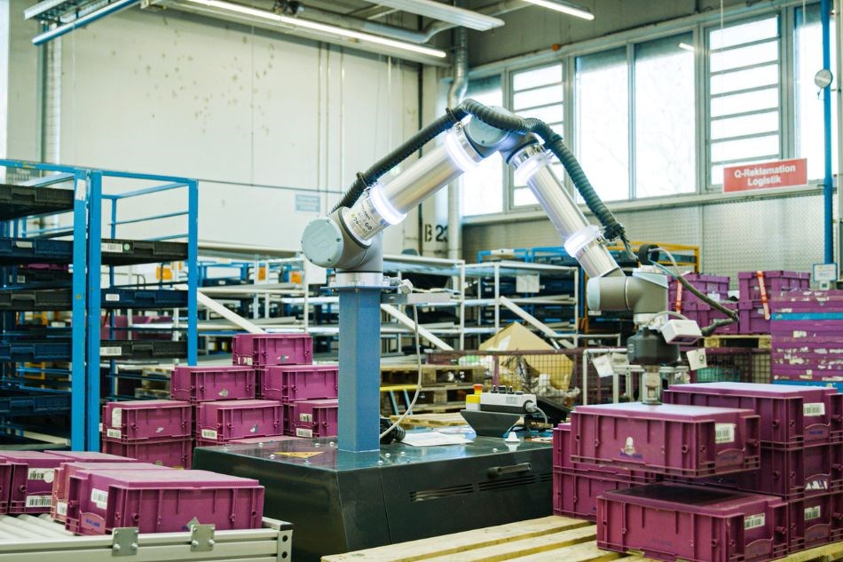 Ein Kollaborierender Roboter stapelt pinke Kisten in einem Lager von BMW.