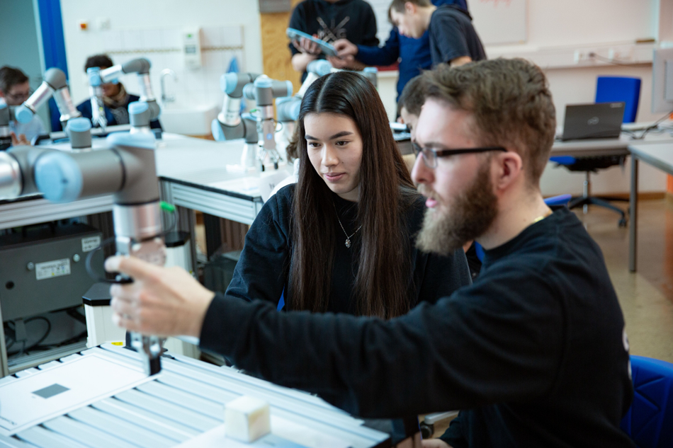 Im Vordergrund sieht man einen Schuler und eine Schülerin, die mit dem Roboter arbeiten.