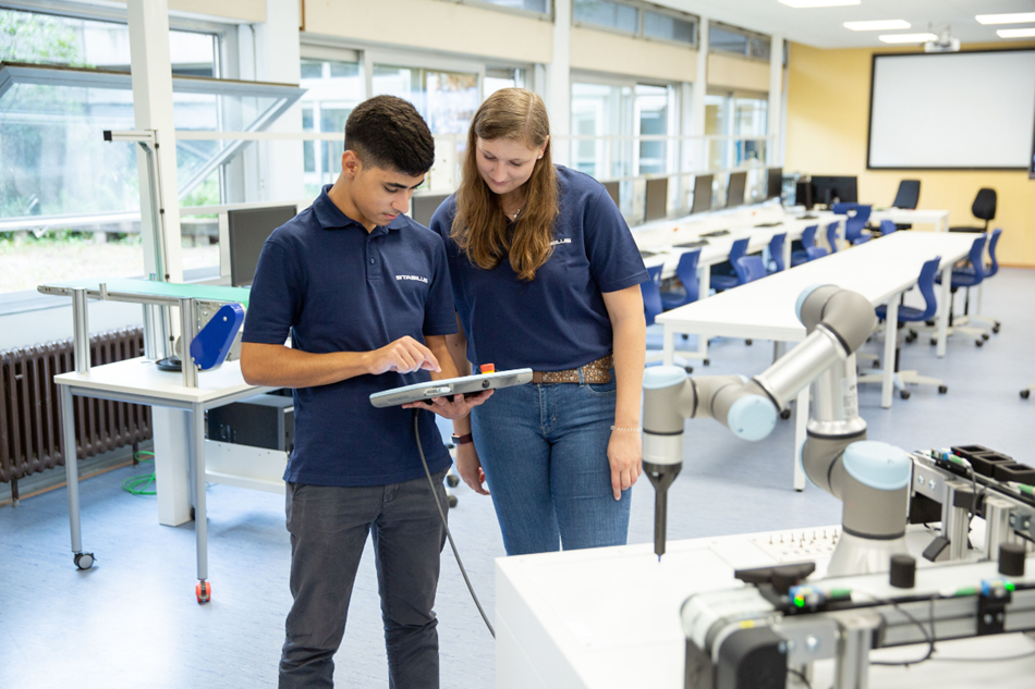Hier sieht man eine Schülerin und einen Schülern, die gerade einen Roboter von Universal Robots programmieren.