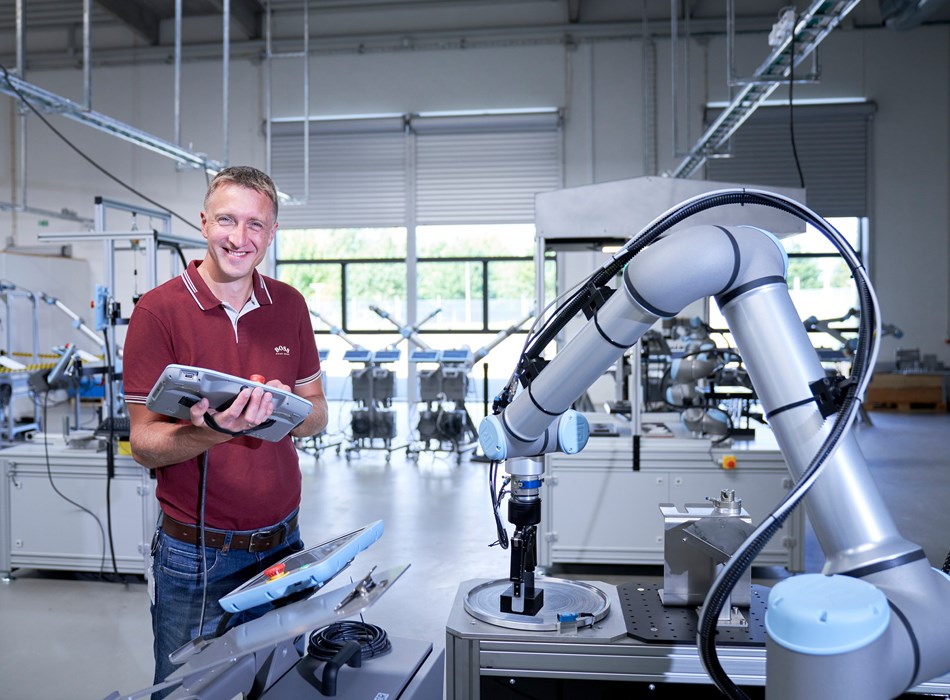 Ein Mitarbeiter ein Teach Pendant in der Hand und lächelt in die Kamera.