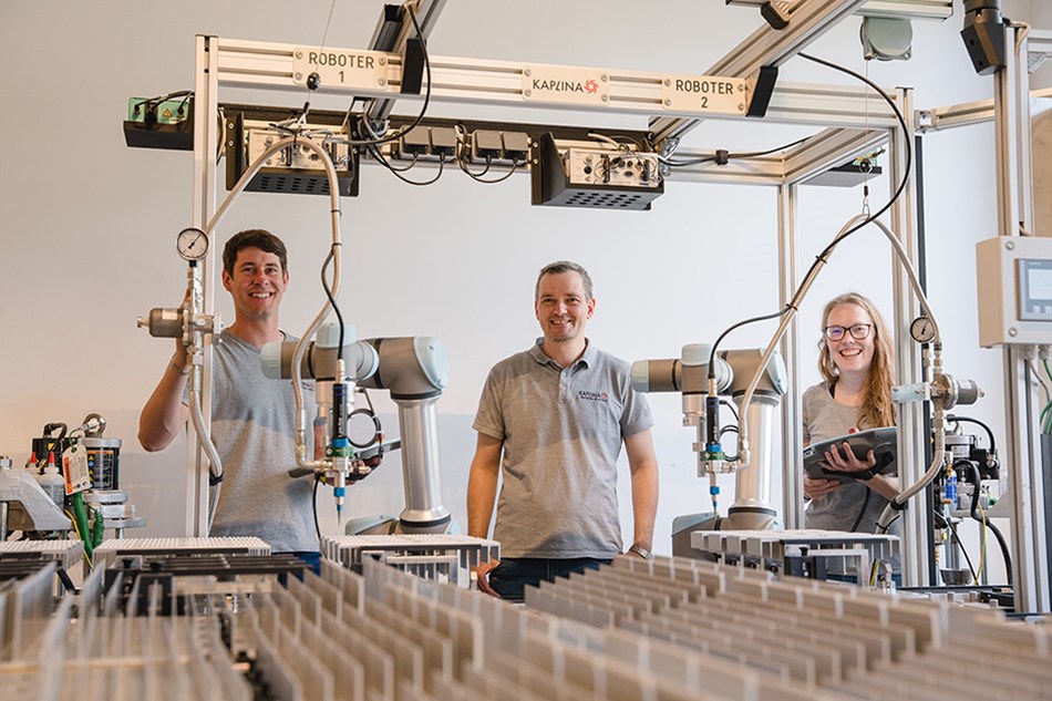 Hier sieht man Geschäftsführer Stefan Bitschnau und seine zwei Robotertechniker Jürgen Meier und Sabrina Auer vor einer Klebeanwendung mit zwei Robotern von Universal Robots.