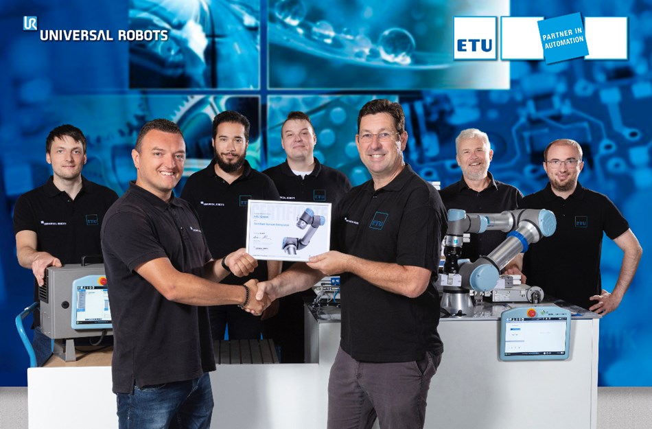Hier sieht man 7 Männer von ETU und Universal Robots, die nebeneinander stehen. Der Mann in der Mitte hält ein Zertifikat.