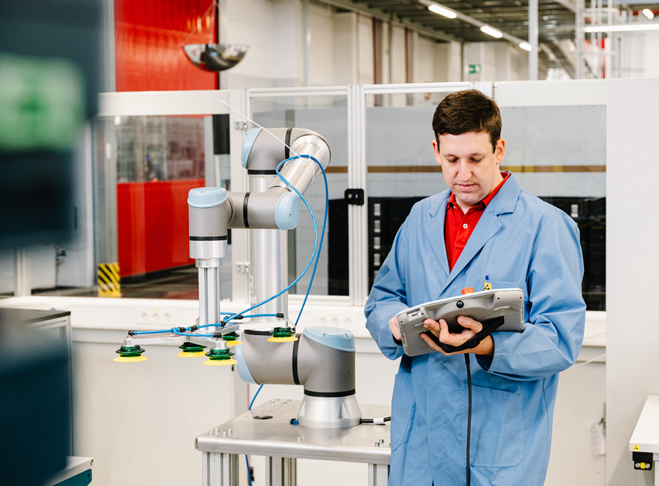 Ein Mitarbeiter steht mit einem Teach Pandent in der Hand neben einem Cobot.