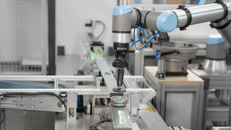 Ein Roboterarm hält ein rundes Bauteile im Greifer und platziert es auf einer Montagestation.